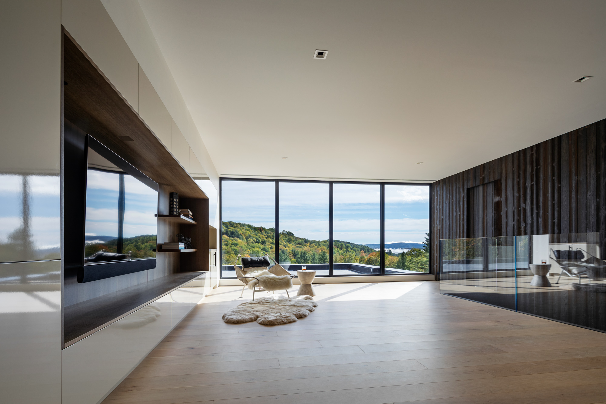 Interior corridor of a modern home with floor-to-ceiling fixed glazing overlooking forest landscape, black aluminium framing