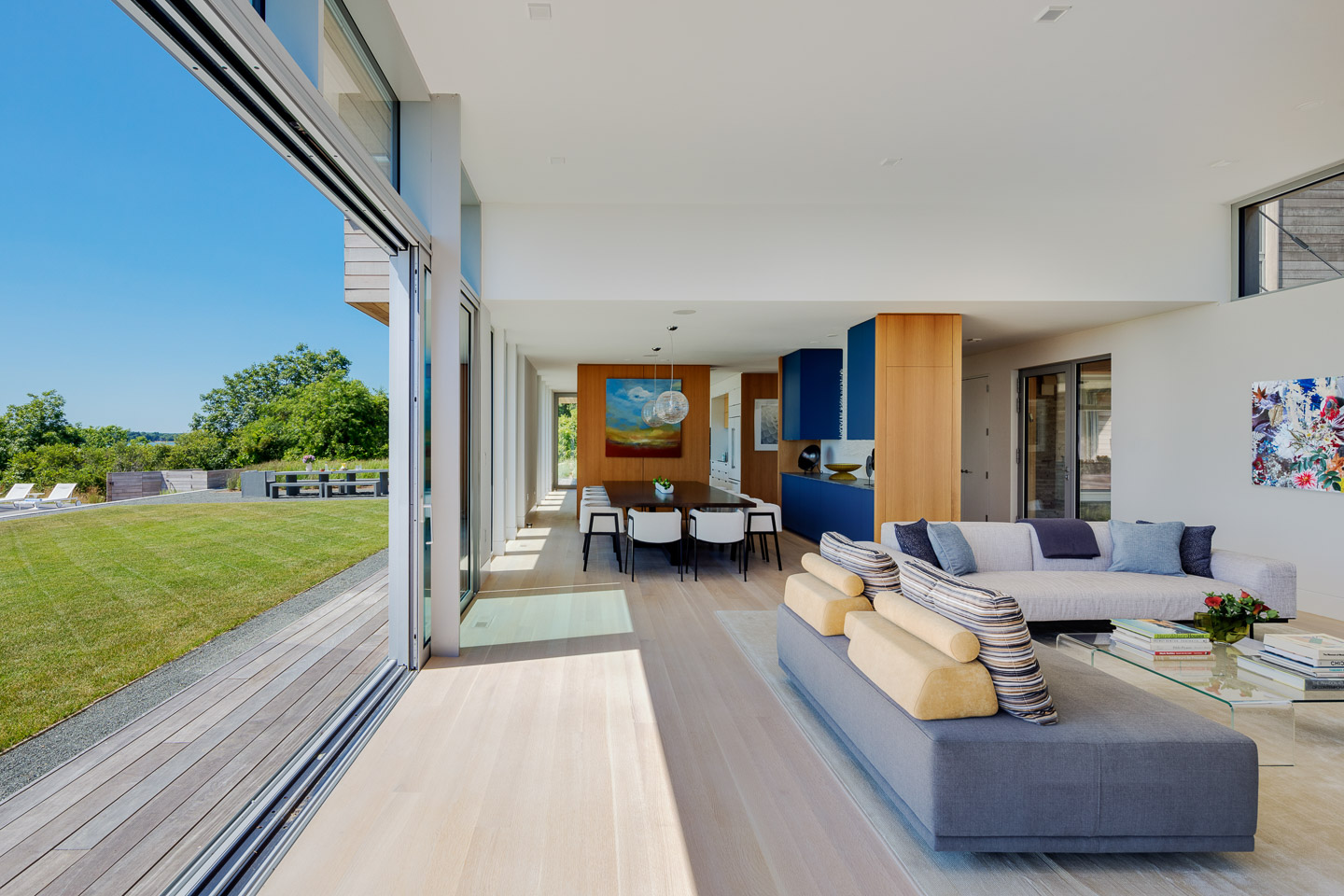 Interior living room with full-width sliding glass wall opening to ocean view, contemporary furnishings